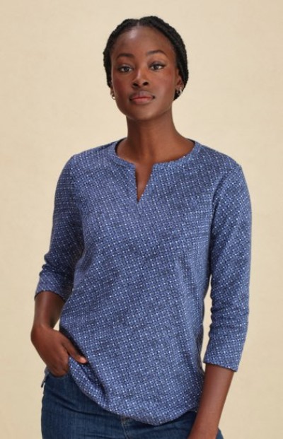 Person in a blue patterned 3/4 sleeve top with a split neckline, paired with denim jeans and hands in pockets.
