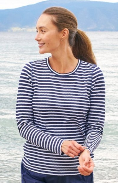 Person in a navy and white striped long-sleeve shirt, standing near a calm waterfront with mountains in the background.