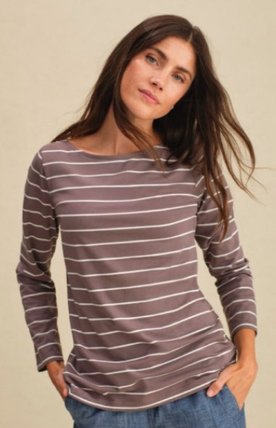 A woman in a brown long-sleeve top with thin white horizontal stripes, paired with blue jeans and hands in pockets.