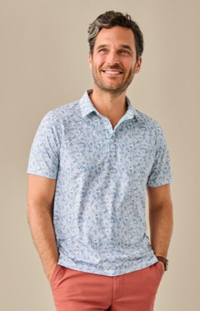 Person wearing a light blue floral-patterned polo shirt paired with coral pants and a brown wristwatch.