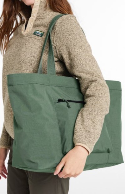 Cropped image of a person wearing a beige fleece carrying a green canvas tote with a zip pocket over their shoulder.