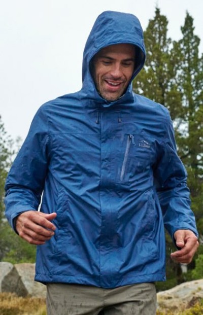 A person in blue hooded rain jacket with zippered chest pocket and hand pockets, designed for outdoor use in wet conditions.