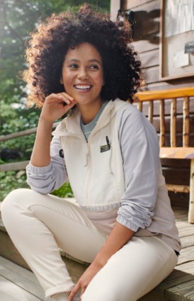 A person in a white pullover jacket with light gray sleeves and a front pocket, sitting outdoors on steps.