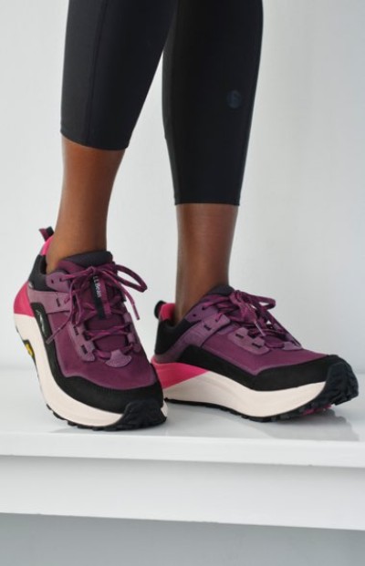 Purple and black trail running shoes with thick white soles, paired with black leggings, shown on a white surface.