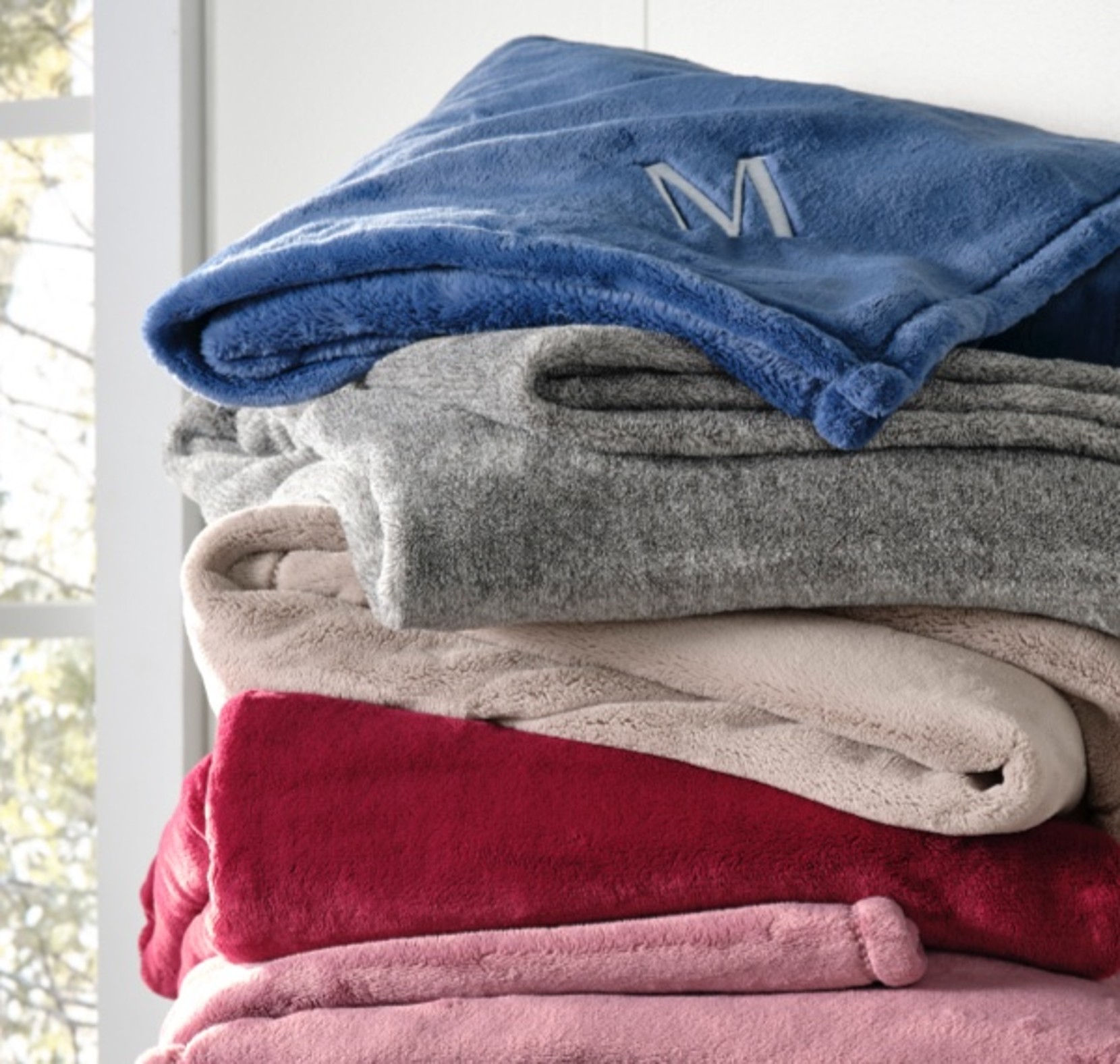 Monogrammed Fleece Throw draped over a colorful stack of fleece blankets