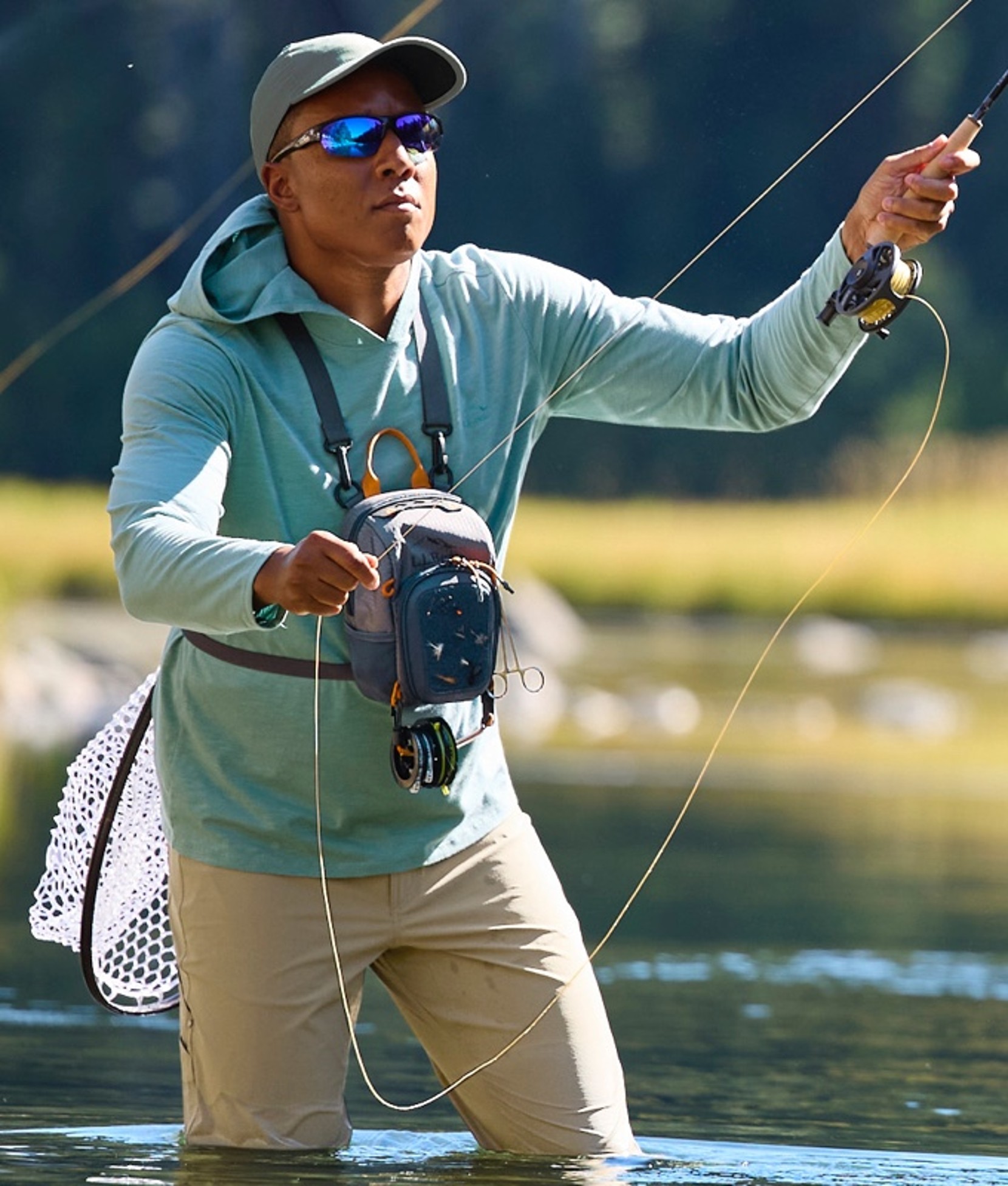 A man fly-fishing, standing in a river up to his knees.