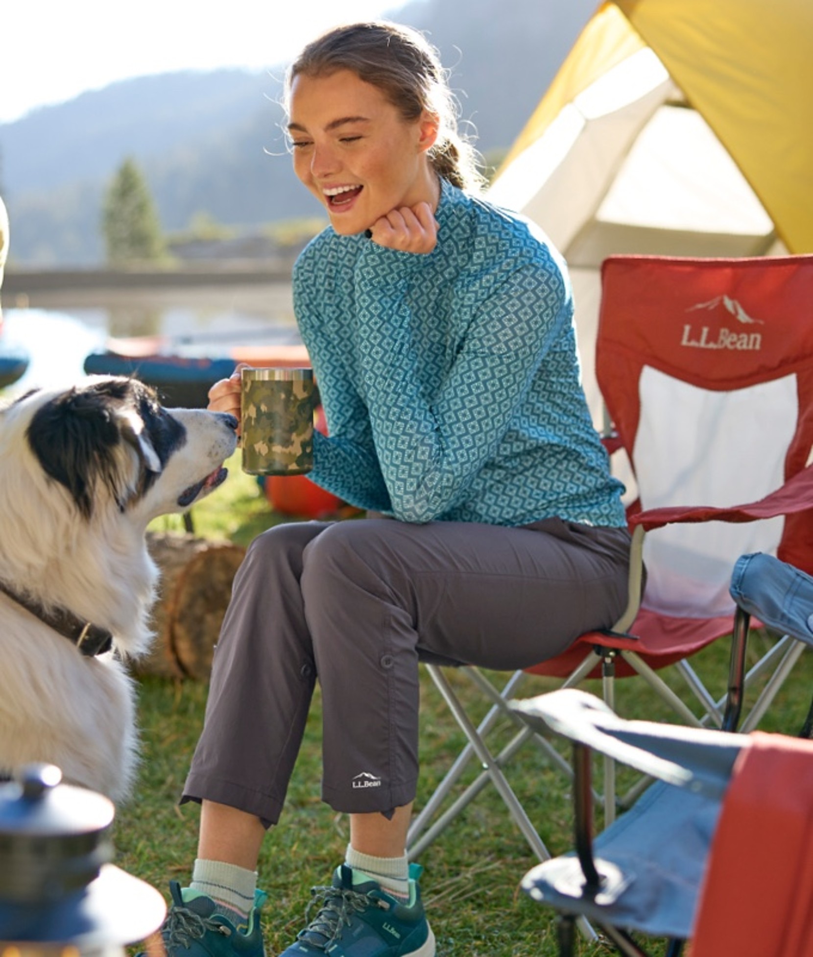 A woman sitting in a camp chair at a camp site, looking at a dog.