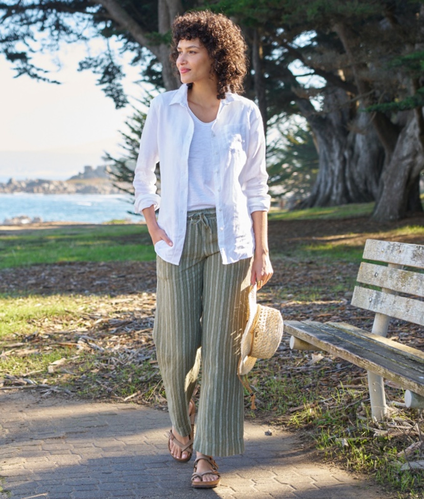 A woman walking outside on a path passing a park bench.