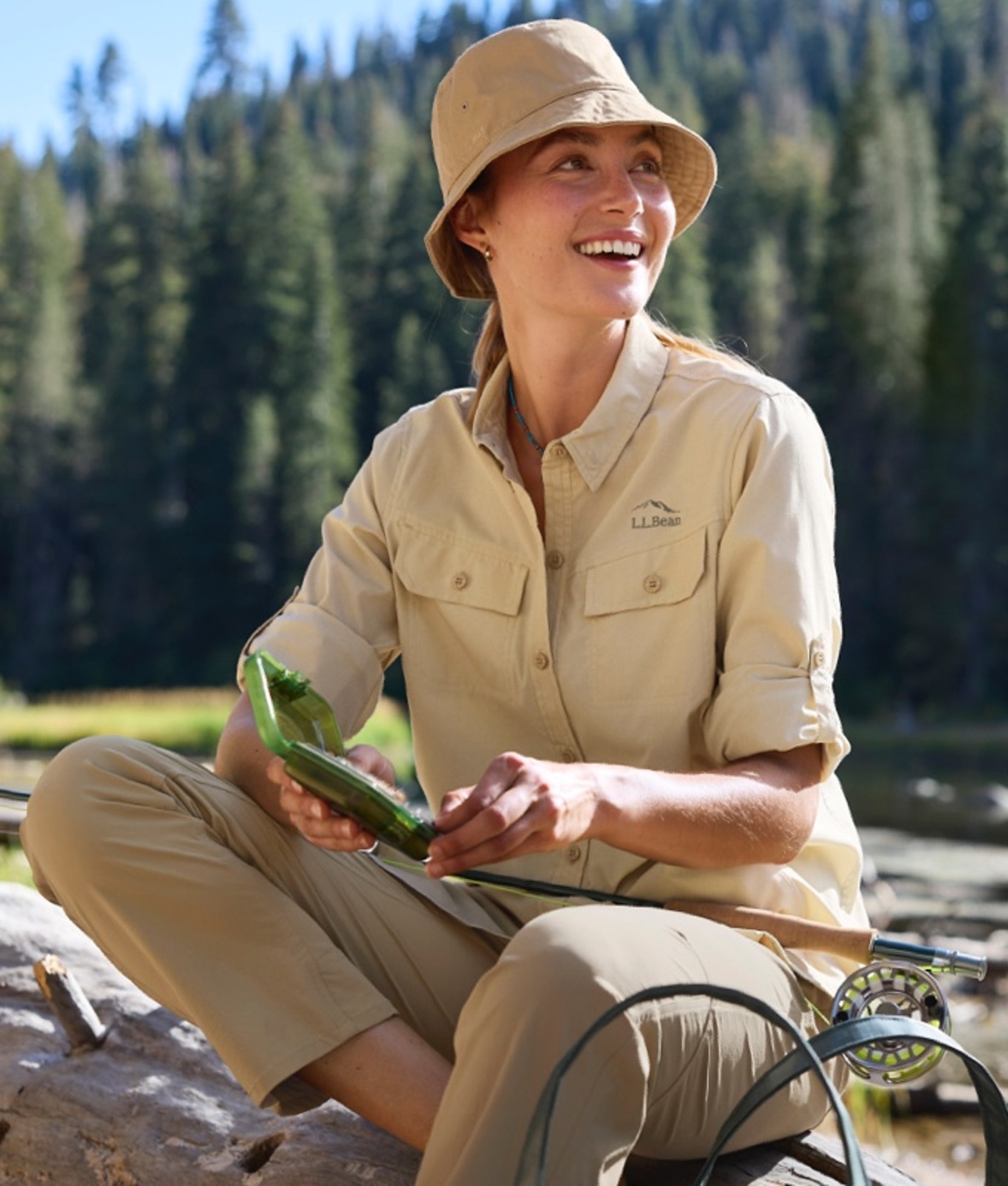 A woman sitting on a rock choosing a fishing fly.