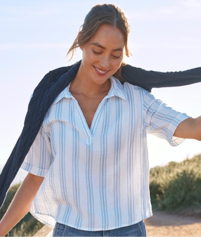Waist-up shot of woman on a beach path, holding the sleeves of a lightweight sweater draped on her shoulders.