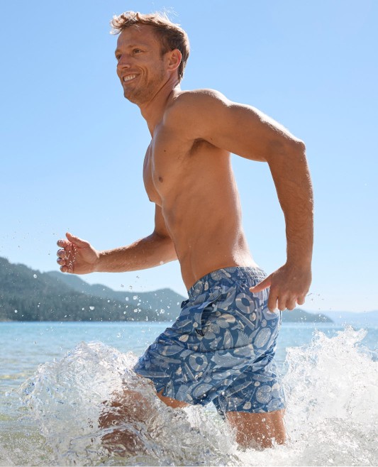 A man running in the surf in swim trunks.