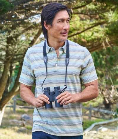 Man wearing a striped polo shirt walking outside with binoculars.