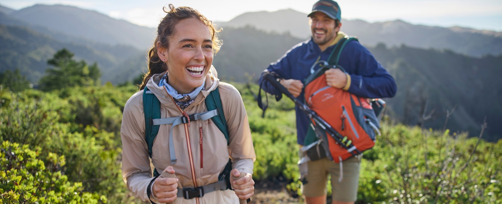 A smiling couple hiking on a rocky trail, hazy mountains in the background.