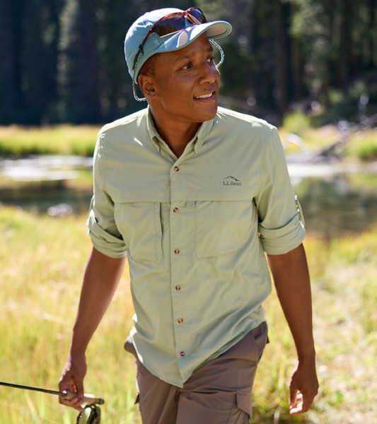 Man holding a fishing rod walking across a field, river in the background.