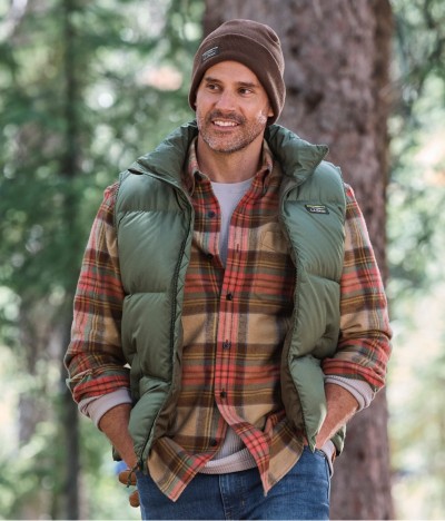 Man in green vest over plaid shirt smiling with hands in pockets. 