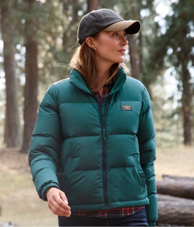 Woman in green puffer jacket and cap looking sideways in woods.