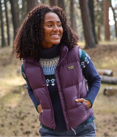 Woman in purple vest and patterned sweater standing in a forest.
