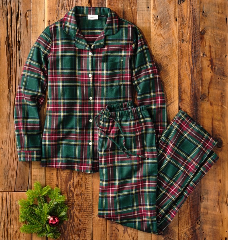 Plaid pajama set laid out on a wooden floor with a pine branch.