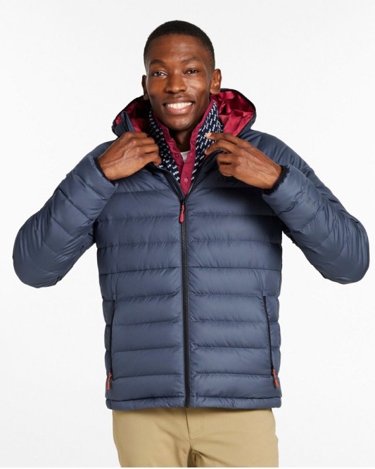 A man wearing a blue puffer jacket with red lining and beige pants, adjusting the collar.