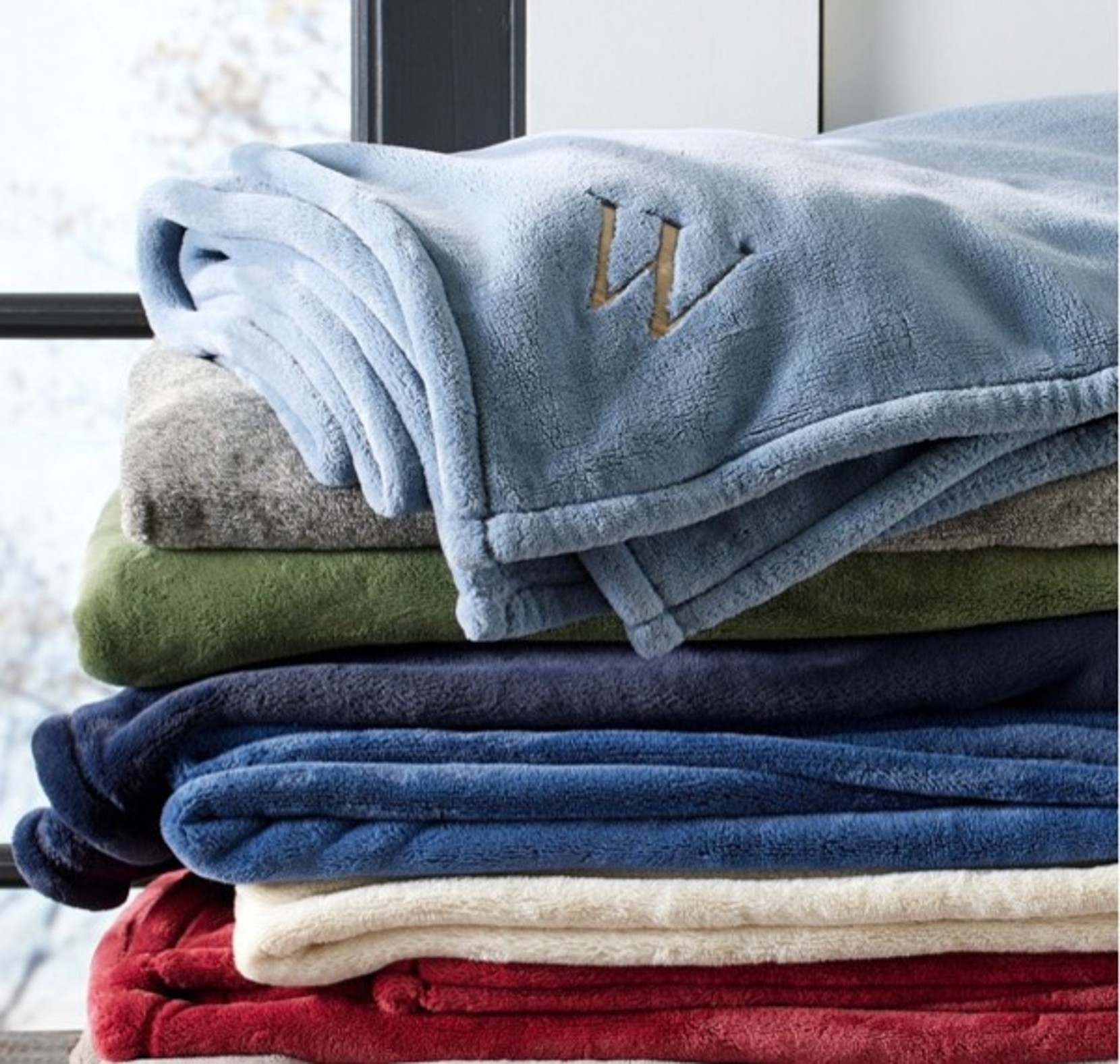 Monogrammed Fleece Throw draped over a colorful stack of fleece blankets