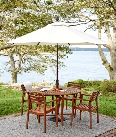 Wooden L. L. Bean patio set with umbrella on a stone deck by a lake, surrounded by trees.