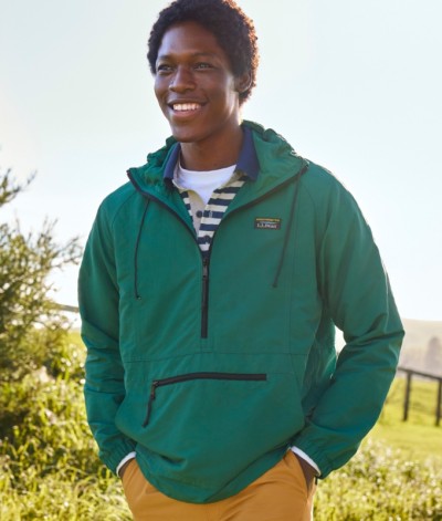 Smiling man in a green anorak pullover with front pocket and striped shirt underneath, standing outdoors.