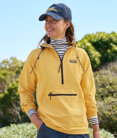Smiling woman in a yellow anorak pullover with front pocket, striped turtleneck, and navy cap, standing outdoors.