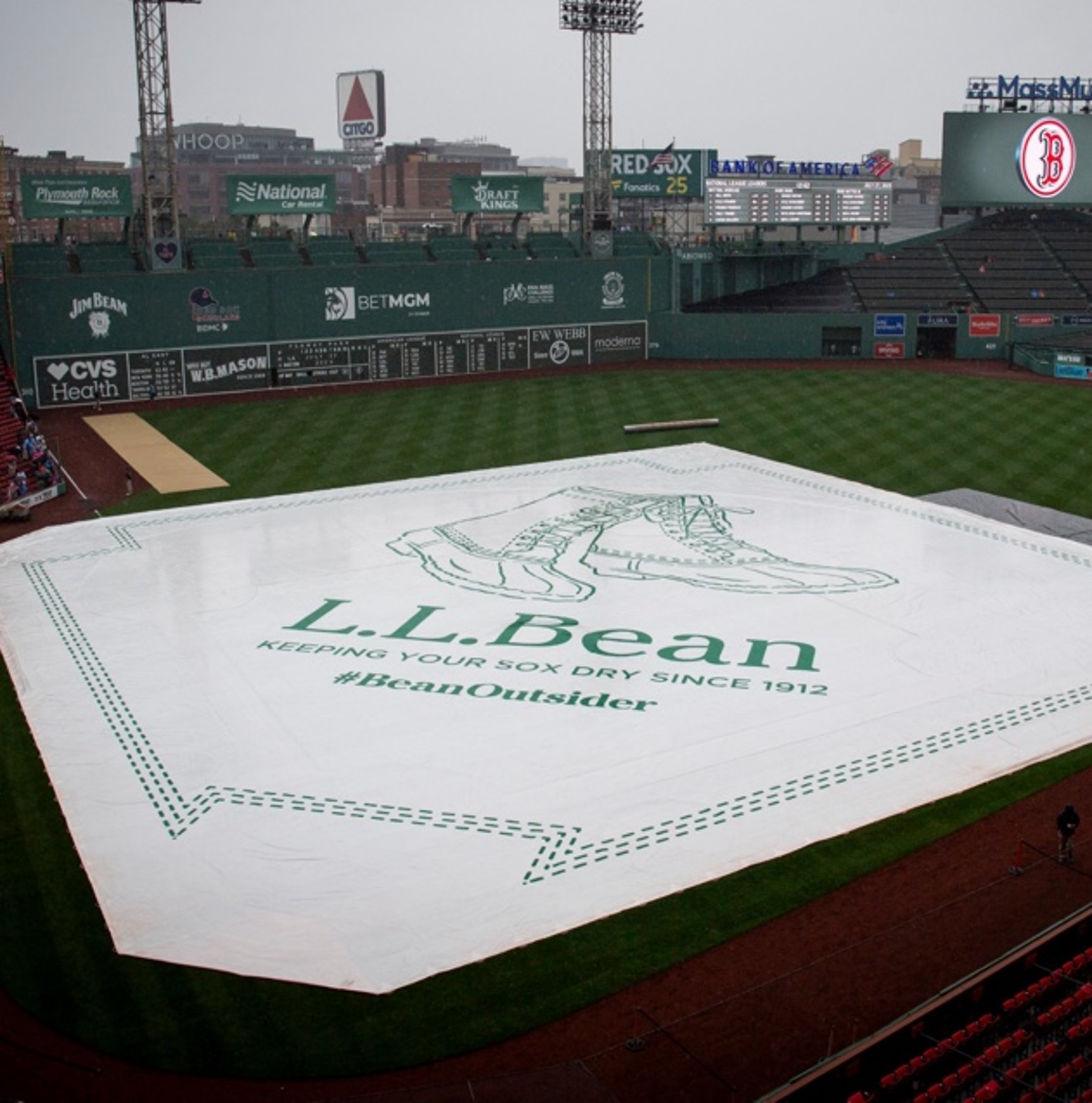 Fenway Park field covered by L.L. Bean tarp with slogan 'Keeping Your Sox Dry Since 1912' and hashtag #BeanOutsider.