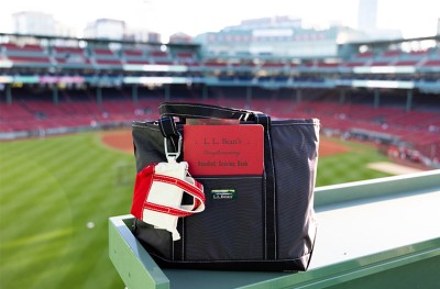Black L L Bean bag with glove and scoring book on ledge overlooking an empty Fenway stadium. 