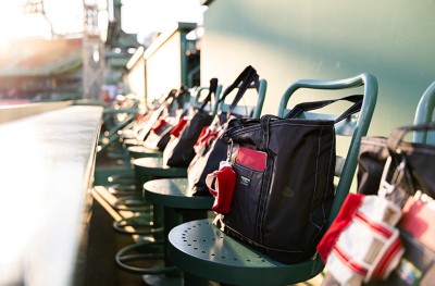 Green stadium seats with black and red bags hanging on them, sunlight shining in from the left side.