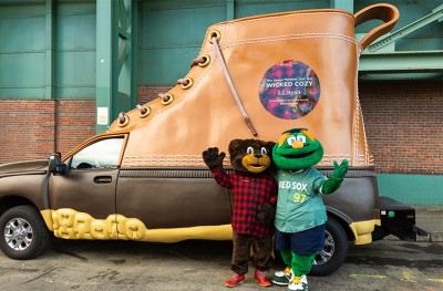Two mascots, L L Bear and a Wally the Green Monster, wave in front of the L L Bean Bootmobile