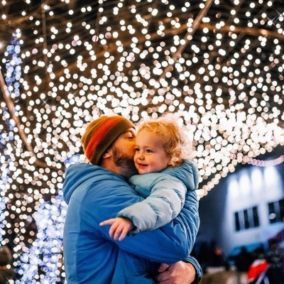 Person in blue jacket holding a child under twinkling lights, creating a festive and cozy atmosphere.