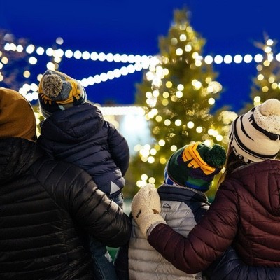 Group in winter clothes admiring a brightly lit outdoor Christmas tree at night.