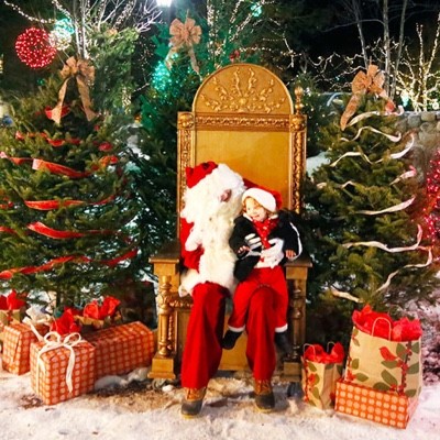 A child sits on Santa's lap, surrounded by wrapped presents and festive holiday decor.