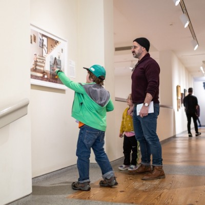 A man and two children in a museum looking at a piece of artwork displayed on the wall.