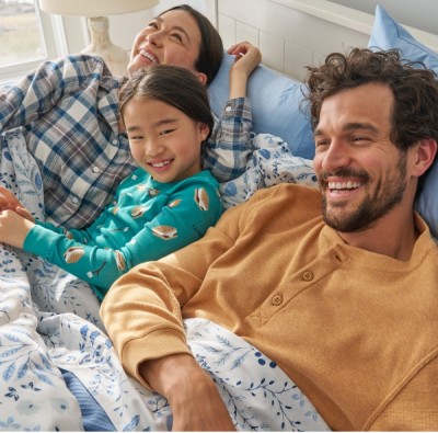 A family wearing pajamas smile as they are all lounging in bed.