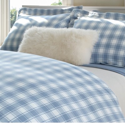 A bed with blue and white plaid bed sheets is neatly folded topped with a white pillow