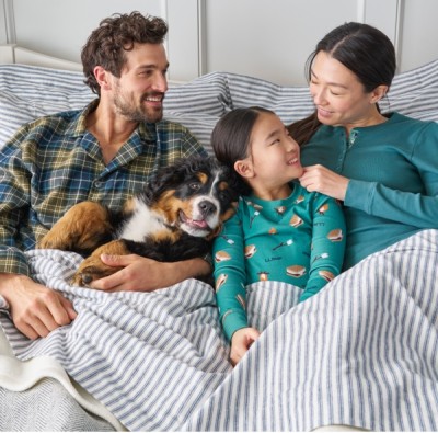 A family along with a dog smile as they are wearing pajamas sitting up in bed.