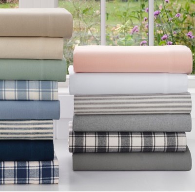 A stack of neatly folded, colorful bed sheets sit in front of a sunny window.