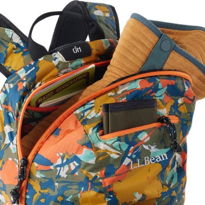 A multi colored pack is open, revealing a orange jacket, sunglasses, and an electronic device. 