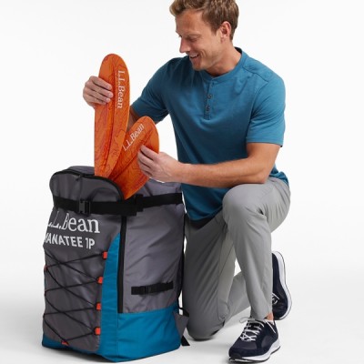 A man in a blue shirt and gray pants places orange paddle parts into a large gray and blue bag.