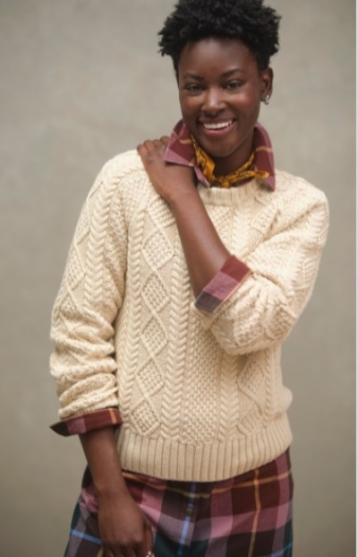 Close up of a woman wearing a plaid shirt layered with a cream colored fisherman sweater.
