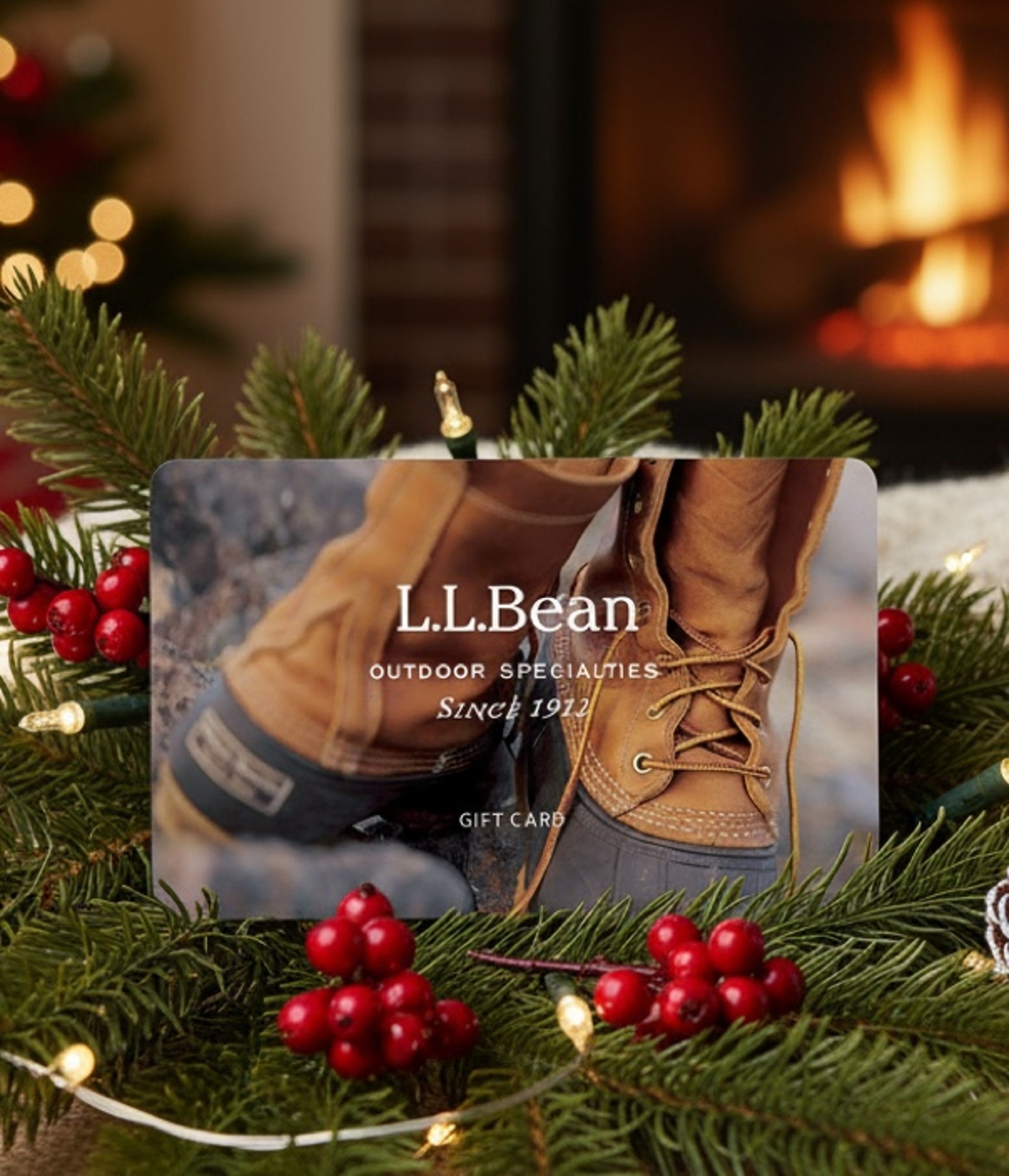 L. L. Bean gift card displayed on festive greenery with red berries and a warm fireplace in the background.