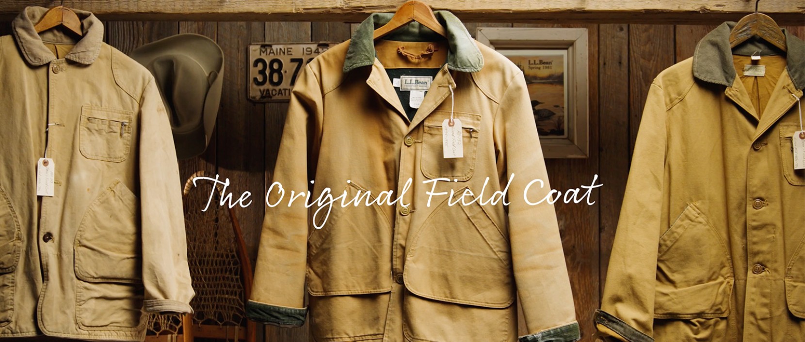 Tan field coat on a hanger in a rustic wooden room with vintage decor and the text ‘The Original Field Coat.’