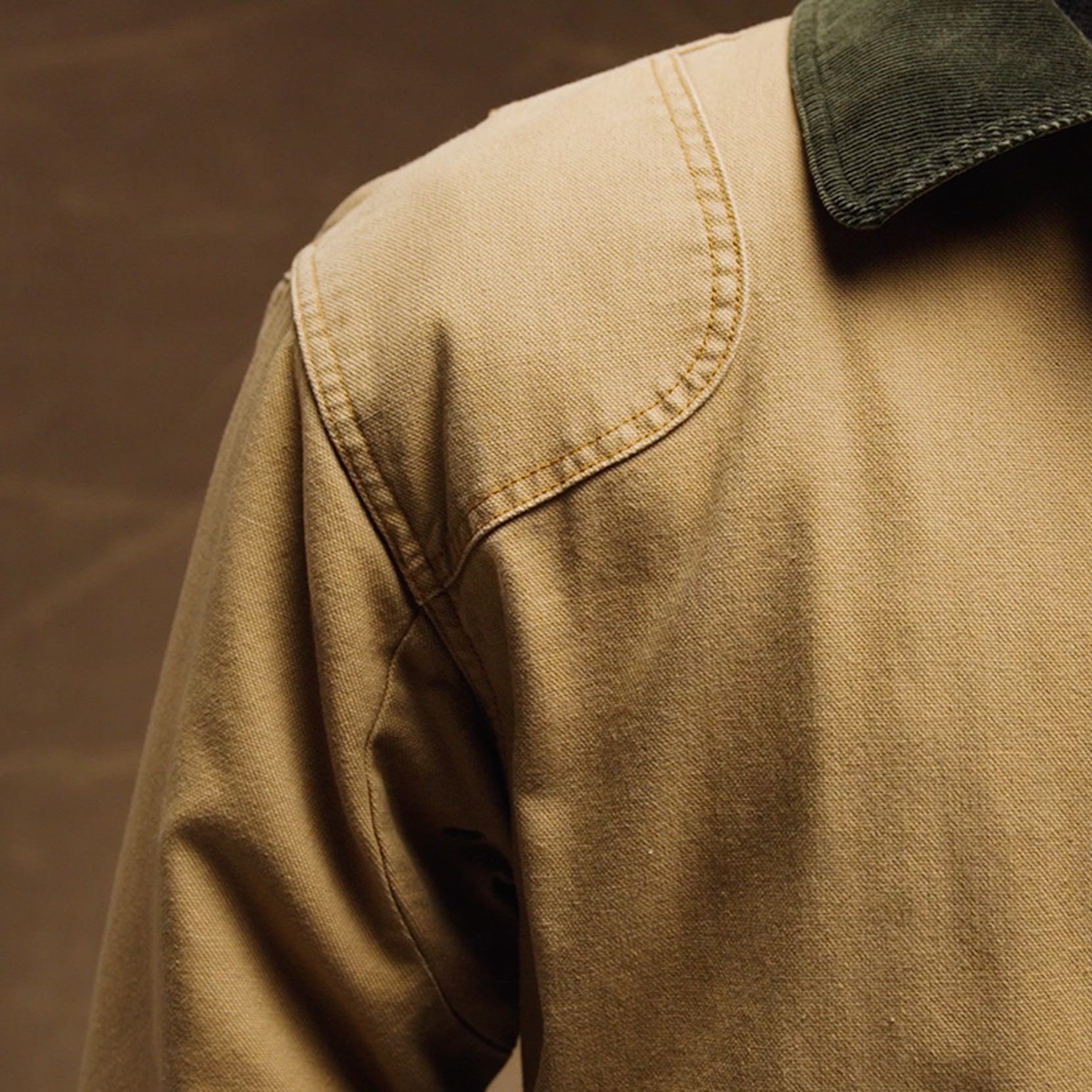 Close-up of a tan field coat shoulder and green corduroy collar against a brown background.