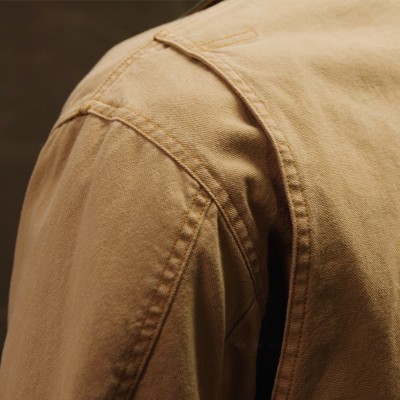 Close up of a tan field coat shoulder and upper sleeve showing stitching and fabric texture.
