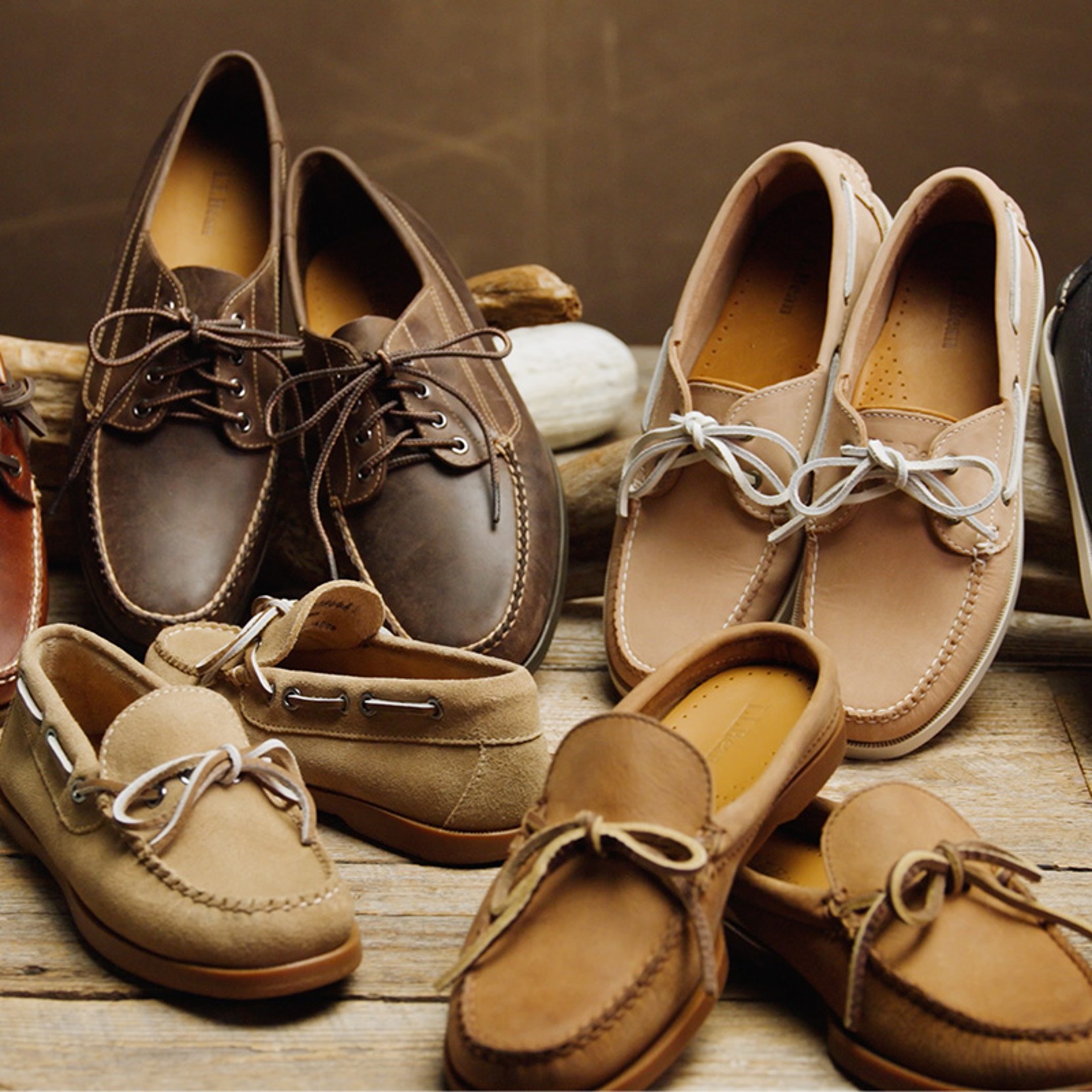 Collection of L L Bean boat shoes in different leather finishes arranged on a rustic tabletop.