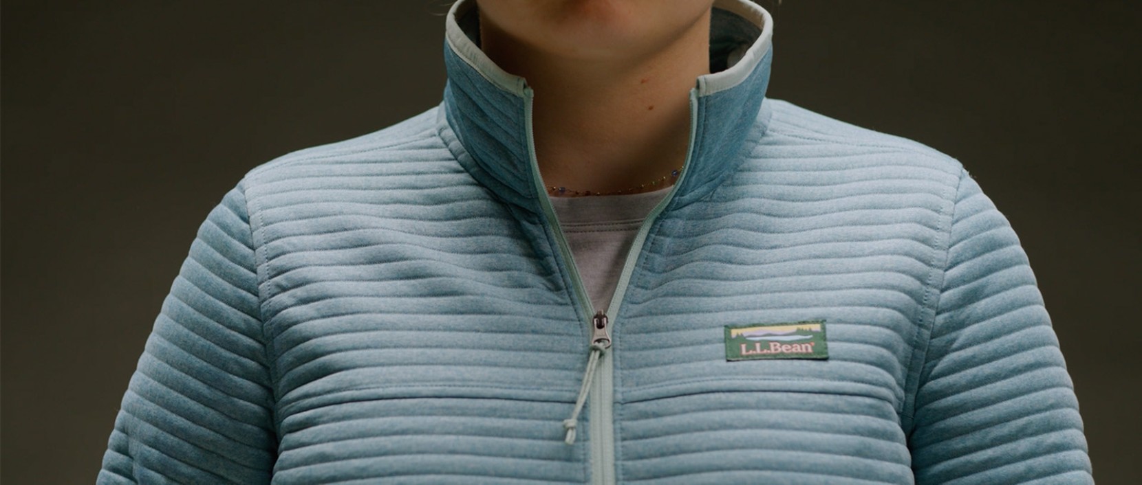 Close-up of a light blue quilted zip jacket with a stand collar and an L L Bean logo patch. 