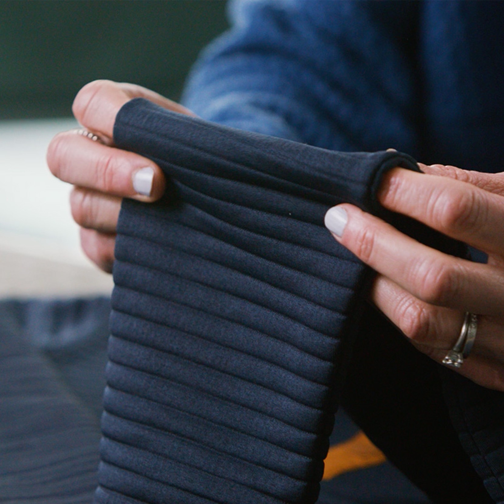 Hands stretch a dark ribbed fabric sleeve to show flexibility and soft texture. 