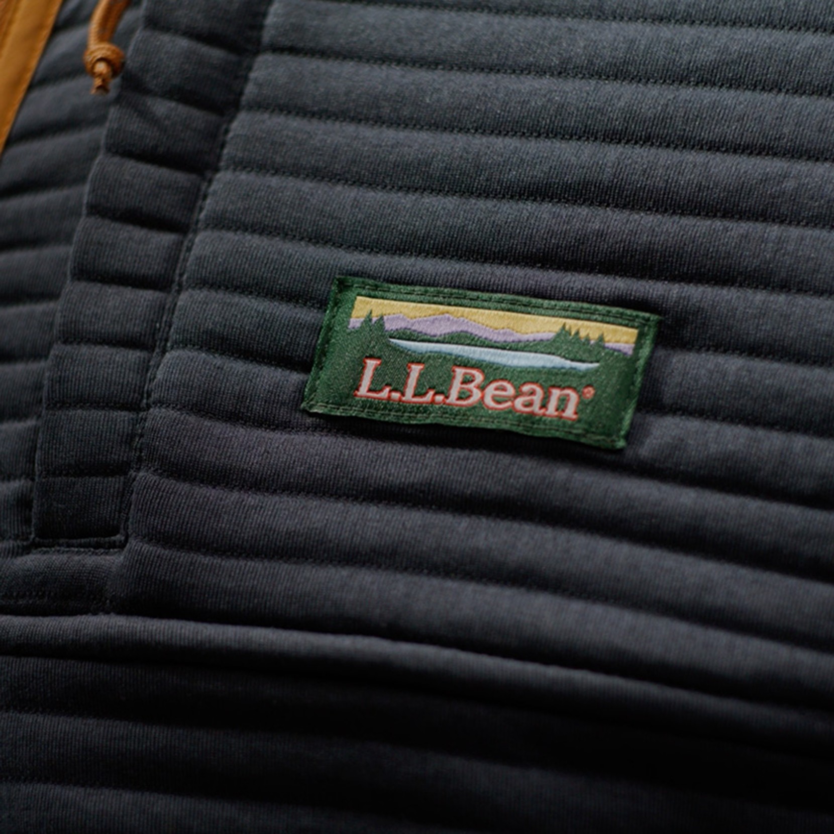 Close-up of a quilted dark jacket panel with an L L Bean logo patch stitched on the chest.
